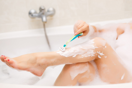 Junge Frau rasiert sich die Beine in der Badewanne